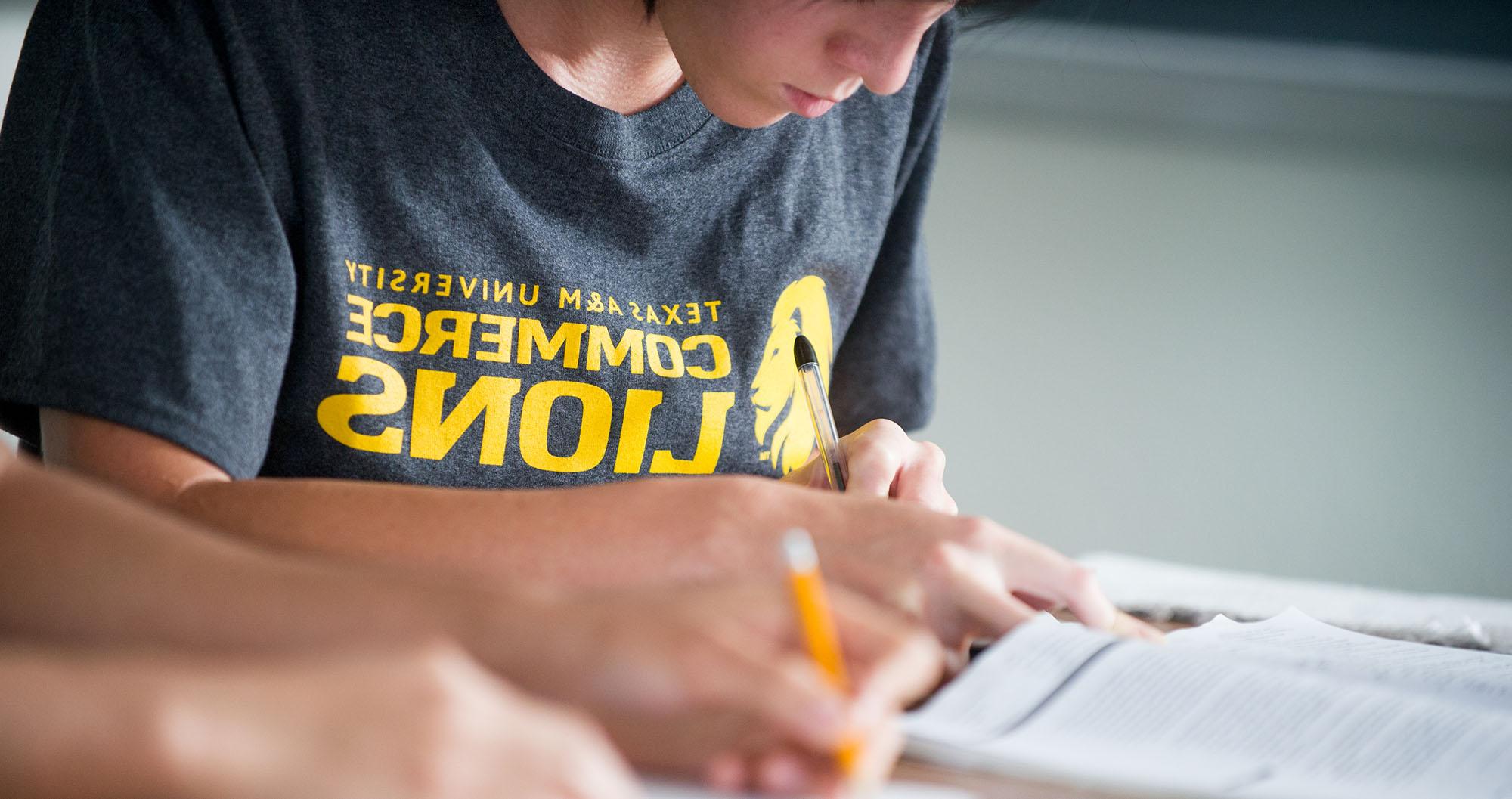 A student completing work wearing a A&M-Commerce t-shirt.